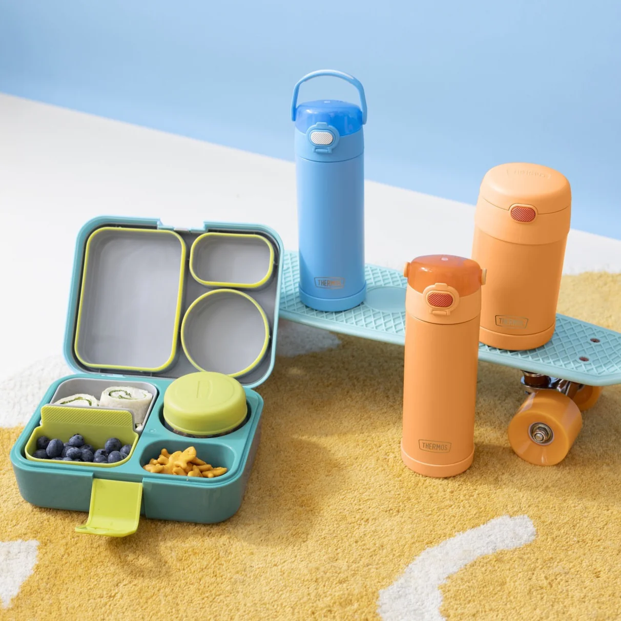 Thermos Funtainer sky blue and neon orange water bottles and neon orange food jar with a packed Freestyle bento-style lunch box.